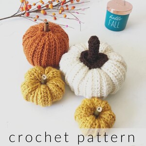May include: Three crocheted pumpkins in different sizes. The largest pumpkin is white, and the two smaller pumpkins are a mustard yellow colour.