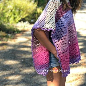 May include: A purple, pink, and white crochet poncho with a scalloped edge. The poncho is worn by a person with long brown hair. The text "Christa Co Design" is visible on the bottom right corner of the image.