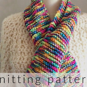 May include: A colorful knitted scarf with a rainbow of colors, including pink, purple, blue, green, yellow, and orange. The scarf is folded in half and draped over a white sweater. The text "knitting pattern" is visible at the bottom of the image.