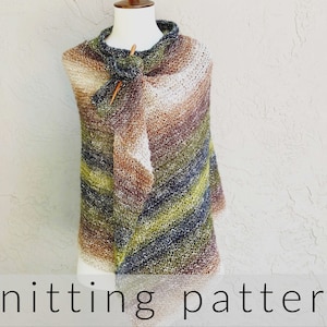 May include: A knitted shawl in shades of brown, green, and white with a subtle speckled texture. The shawl is draped over a white mannequin and is pinned with a wooden knitting needle.