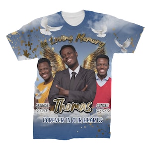 May include: A blue t-shirt with a white background and a memorial design. The design features a photo of a man with angel wings, two doves, and the text "In Loving Memory Thomas, Forever in Our Hearts". The dates "Sunrise 03/11/63" and "Sunset 01/10/15" are also included.