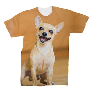 May include: A brown and white chihuahua dog with a happy expression on a tan t-shirt.