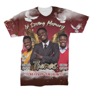May include: A red, white, and gold t-shirt with a memorial design. The shirt features a photo of three people, two doves, and the text "In Loving Memory Thomas Forever In Our Hearts". The shirt also includes the dates "Sunrise 03/11/83 Sunset 02/10/15".