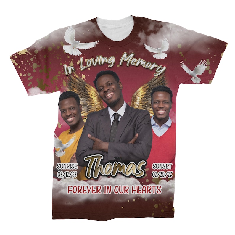 May include: A red, white, and gold t-shirt with a memorial design. The shirt features a photo of three people, two doves, and the text "In Loving Memory Thomas Forever In Our Hearts". The shirt also includes the dates "Sunrise 03/11/83 Sunset 02/10/15".