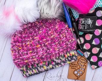 May include: A handmade pink and gray knit hat with a faux fur pom-pom. The hat is surrounded by knitting supplies, including yarn, crochet hooks, and fabric with a hedgehog pattern. The image also includes a wooden gauge and a label that says "Molly Girl".