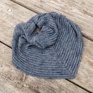 May include: A blue and gray knitted scarf with a ribbed texture. The scarf is folded in half and is lying on a wooden surface.