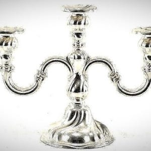Pode incluir: Um castiçal prateado com três braços, cada um com um suporte para vela. A base é ornamentada com uma borda ondulada. Os braços curvam-se graciosamente da coluna central. O castiçal é feito de metal brilhante e reflexivo.