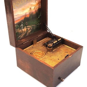 May include: A vintage wooden music box with the word "POLYPHON" on the inside lid. The lid features a painted landscape scene. The box is open, revealing the internal mechanism and a gold-colored soundboard. A small knob is visible on the side.
