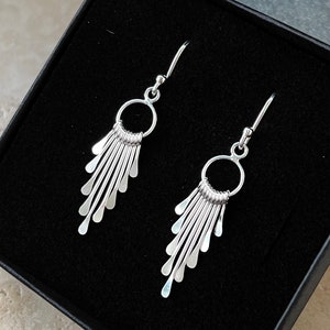 May include: A pair of silver dangle earrings with a circle design and multiple thin, silver strands hanging down.