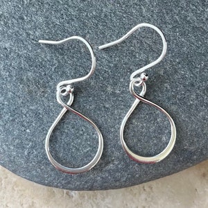 May include: A pair of silver dangle earrings with a simple, twisted, teardrop shape.