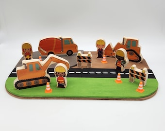May include: A wooden playset with a construction theme. The set includes a cement mixer, an excavator, a bulldozer, two construction workers, and two traffic cones. The playset is on a brown wooden base with a green grass area.