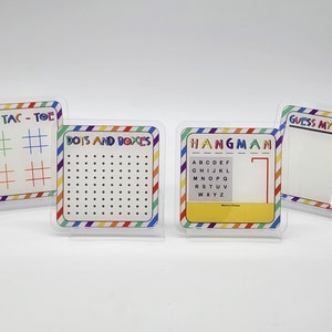 May include: Four colorful dry-erase boards with different games: Tic-Tac-Toe, Dots and Boxes, Hangman, and Guess My Sketch. Each board has a rainbow striped border.