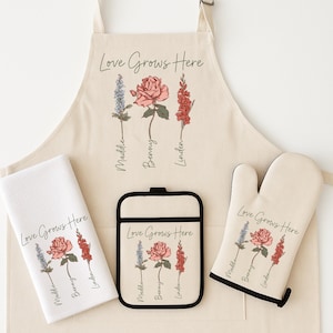 Peut inclure: Un ensemble de cuisine beige comprenant un tablier, une manique, un dessous-de-plat et un torchon. Chaque article est imprimé avec la phrase "Love Grows Here" et des illustrations florales de fleurs bleues, roses et rouges. Les noms "Maddie", "Benny" et "Linden" sont imprimés.