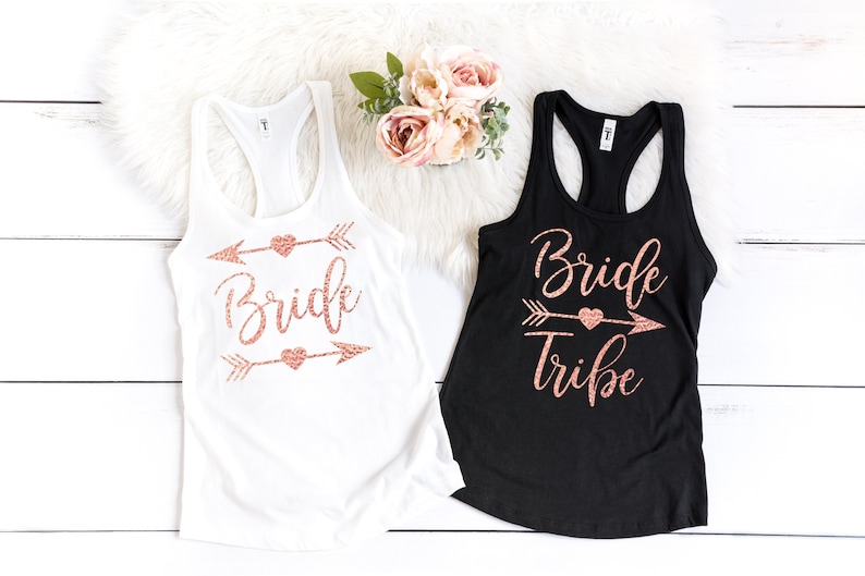 May include: Two tank tops with rose gold glitter text and arrow designs. One white tank top says "Bride" and the other black tank top says "Bride Tribe".
