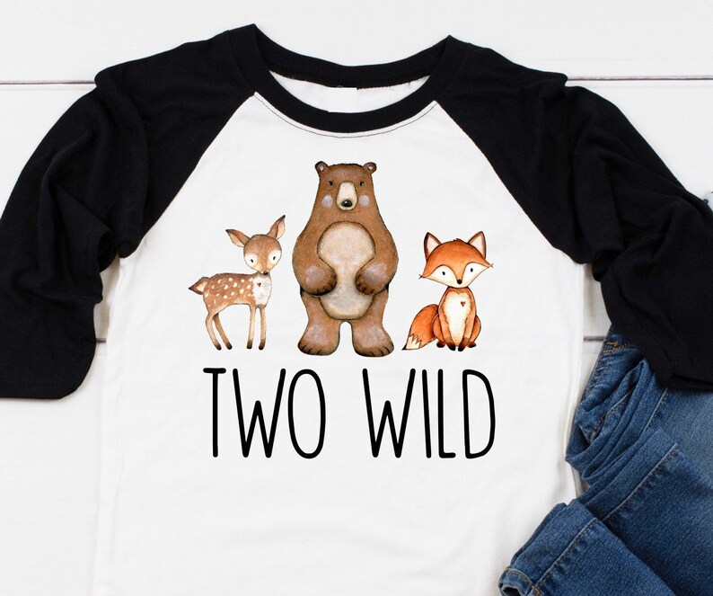 May include: A white and black baseball tee shirt with a brown bear, a deer, and a fox. The shirt says "Two Wild" in black text.
