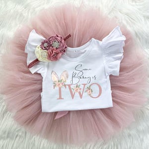 May include: A pink tulle tutu skirt and a white short-sleeved top with a pink bunny graphic and the text "Some Bunny is Two".