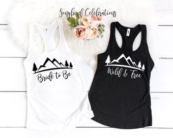 May include: Two white tank tops with black mountain and tree graphics. One tank top says "Bride to Be" and the other says "Wild & Free".