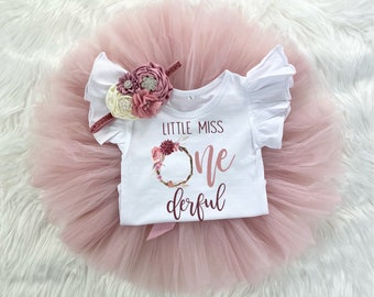 May include: A white onesie with a pink floral wreath and the text "Little Miss One-derful". The onesie is paired with a pink tulle tutu.