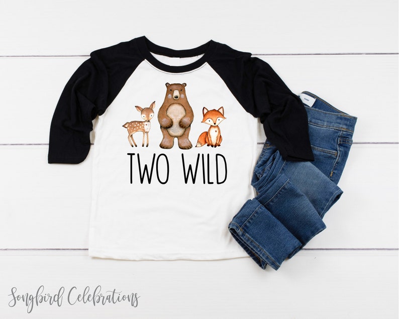 May include: White and black baseball tee shirt with a brown bear, a deer, and a fox graphic. The text "TWO WILD" is printed below the animals.