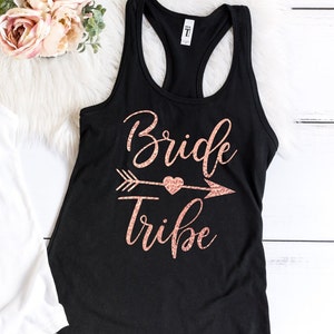 May include: Black tank top with a rose gold glitter design that says "Bride Tribe" with an arrow and heart.