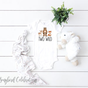 May include: White baby onesie with a brown bear, deer, and fox illustration. The text "TWO WILD" is printed in black below the animals.