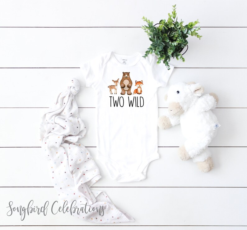 May include: White baby onesie with a brown bear, deer, and fox illustration. The text "TWO WILD" is printed in black below the animals.