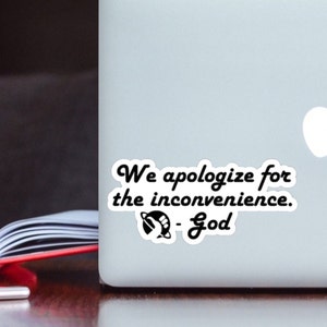 Op de afbeelding: Een witte sticker met zwarte tekst die "We apologize for the inconvenience. - God" luidt, met een zwart-witte afbeelding van een planeet en een hand.