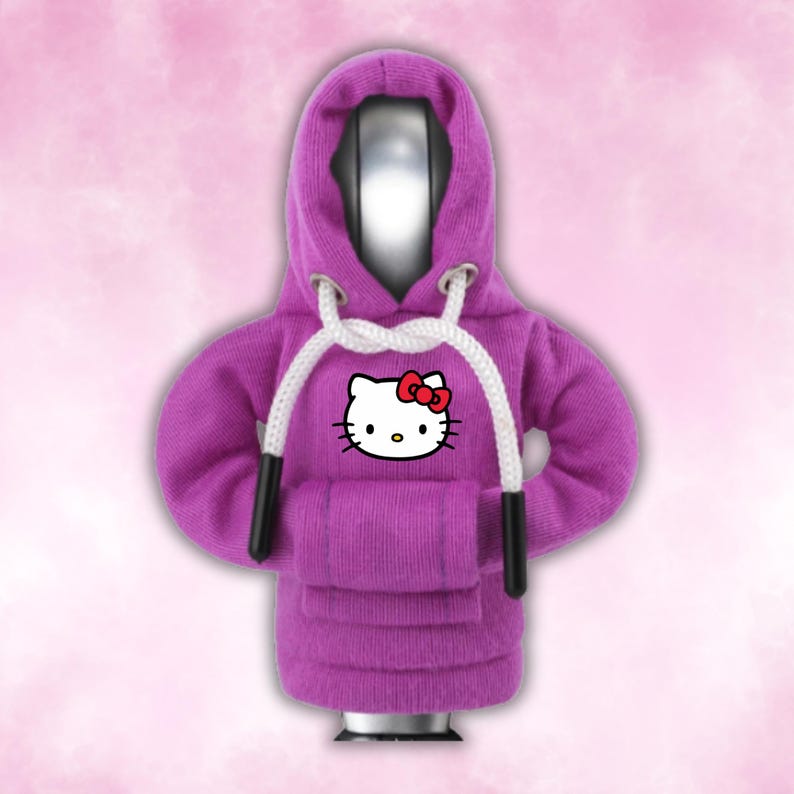 May include: Purple hooded sweatshirt with a white Hello Kitty graphic on the front. The hoodie has a white drawstring and black drawstrings.