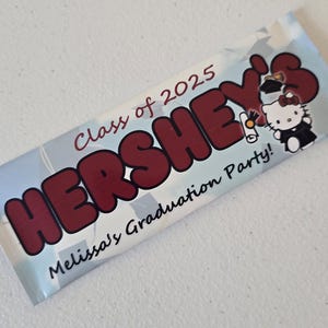 May include: A blue and white Hershey's chocolate bar wrapper with the text "Class of 2025" and "Melissa's Graduation Party!"  A cartoon image of Hello Kitty wearing a graduation cap is on the wrapper.