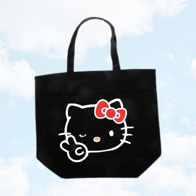 May include: Black tote bag with a white outline of Hello Kitty giving the peace sign. Hello Kitty is wearing a red bow.