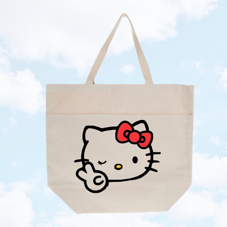 May include: A white canvas tote bag with a black and red Hello Kitty design. Hello Kitty is winking and giving the peace sign.
