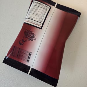 May include: A red and white graduation party favor bag with a black border. The bag has a list of graduation facts with a 100% rating for each item. The text on the bag reads "Graduation Facts" and "Thank you for coming to [Name]'s Graduation Party".