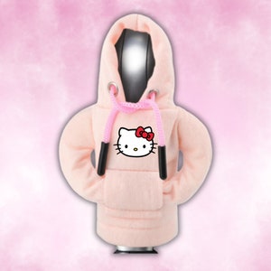 May include: A pink hoodie with a white Hello Kitty graphic on the front. The hoodie has a drawstring and a kangaroo pocket.