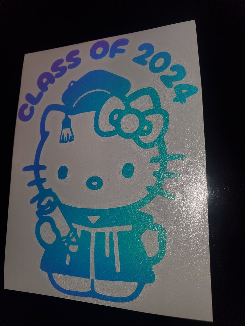 May include: A blue and purple gradient vinyl sticker featuring Hello Kitty dressed in a graduation cap and gown, holding a diploma. The sticker says "Class of 2024" around the top.