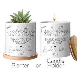 May include: White ceramic planter and candle holder with the text "Godmothers are a blessing. Thank you for being mine. Easton John 2024." The planter holds a succulent, and the candle holder has a lit candle. Both sit on a wooden base.