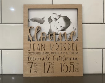 May include: A wooden photo frame with a cutout of the name "Sloane" and the text "JEAN KRISPEL, OCTOBER 26, 2021 AT 4:15PM, Oceanside, California, 7 pounds 12 ounces 16.5 inches". A black and white photo of a baby is in the frame.