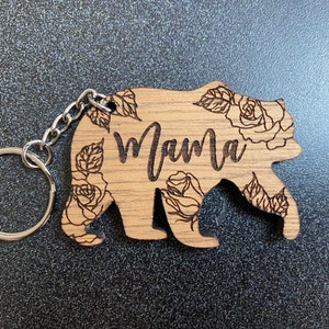 May include: Wooden bear keychain with a floral design and the word "Mama" engraved on it.