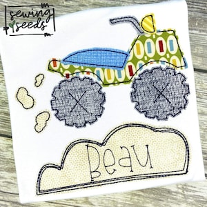 May include: A green and blue monster truck with the name "Beau" embroidered on a beige cloud. The truck has large black tires and is surrounded by small white clouds.