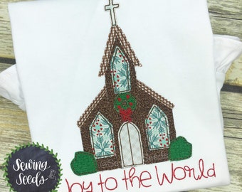 May include: Embroidered design of a brown church with a red wreath on the front and the text "Joy to the World" in red thread. The design is on a white t-shirt.