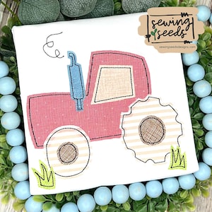 May include: A red and white tractor with a blue exhaust pipe and green grass. The tractor is embroidered on a white t-shirt. The design is from Sewing Seeds Designs.