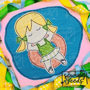Puede incluir: Diseño bordado de una niña con cabello rubio y coletas que lleva un traje de baño verde y blanco y flota en un flotador rojo y naranja. El diseño está sobre un fondo de tela rosa.