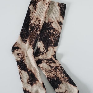 Może przedstawiać: Para białych skarpet z czarnym wzorem rozpryskanym wybielaczem.