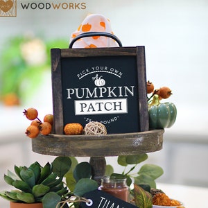 Puede incluir: Una bandeja de madera de dos niveles decorada con artículos de temática otoñal, que incluyen una pequeña calabaza, una planta suculenta, una vela y un letrero que dice "Pick Your Own Pumpkin Patch .25/Pound". La bandeja también tiene una etiqueta de pizarra negra que dice "Thankful".