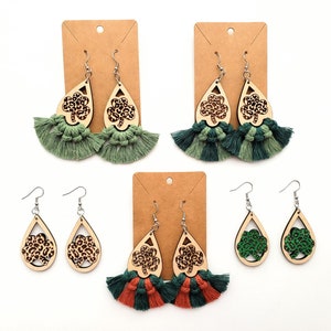 May include: Three pairs of dangle earrings with a shamrock design. The earrings are made of wood and have a green, orange, and brown color scheme. The earrings are accented with tassels.