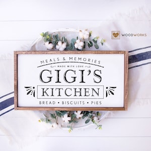 May include: A wooden sign with the text "Meals & Memories Made With Love Gigi's Kitchen Bread Biscuits Pies" in black lettering on a white background. The sign is framed in brown wood.