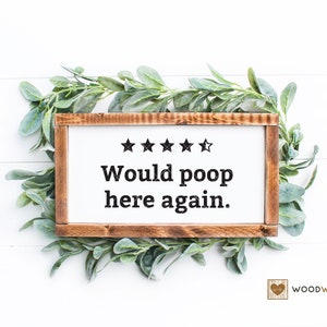 Peut inclure: Une pancarte en bois blanc avec un cadre brun, comportant cinq étoiles et le texte "Would poop here again." La pancarte est entourée de feuillage vert sur un fond blanc. Le texte "WOODWORKS" est visible dans le coin inférieur droit.