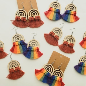 May include: Rainbow colored tassel earrings with wooden rainbow arch designs. The earrings are made with a variety of colors, including red, orange, yellow, green, blue, indigo, and violet.