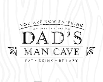 May include: Black and white sign with the text "You are now entering Dad's Man Cave. Open 24 hours. Eat. Drink. Be Lazy."  The sign has a woodgrain background and a small heart with the word "Woodworks" below it.