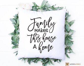 May include: White throw pillow with black text that reads "Family makes this house a home". The pillow is surrounded by a green leafy garland.