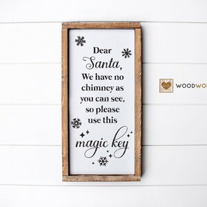 May include: A white wooden sign with a brown frame, featuring the text "Dear Santa, We have no chimney as you can see, so please use this magic key." The sign is decorated with snowflakes and stars.